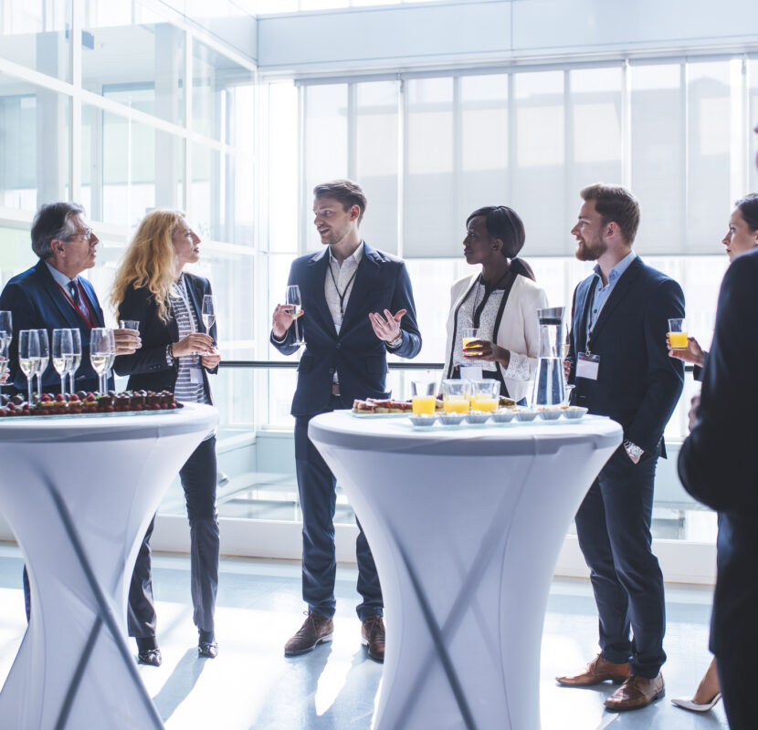 Business coworkers standing in a lobby. They are looking at each other and holding glasses of champagne and juice.